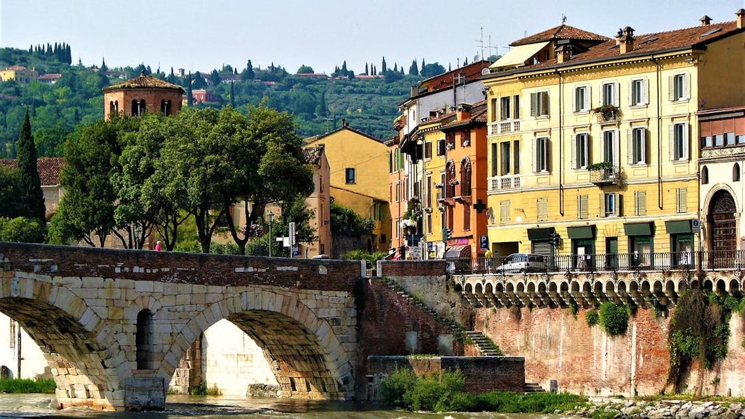 Verona's Ponte Pietra bridge with colorful buildings and lush greenery in the background.