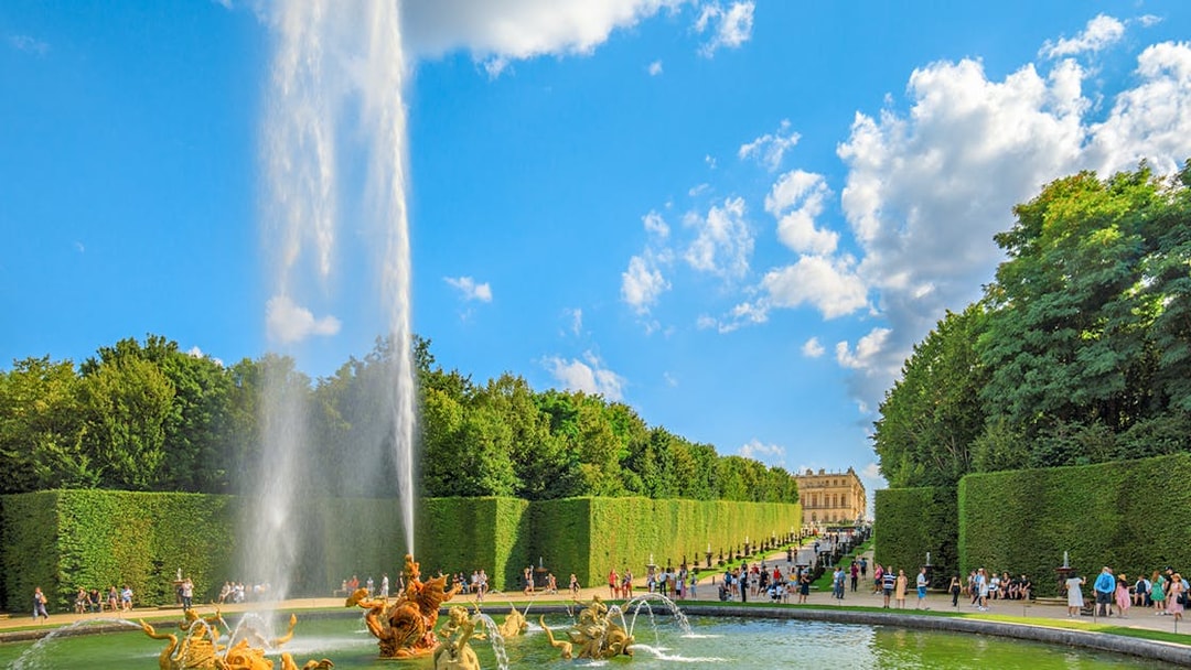 Fountain at Dragon Basin, Versailles, with visitors and palace in background.