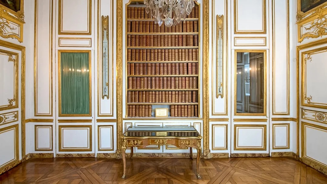 Bookshelf and ornate table in the Palace of Versailles library room.