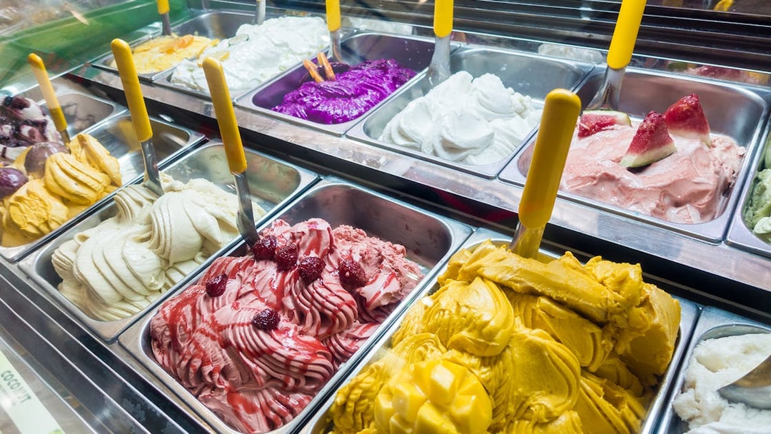 Assorted colorful gelato flavors in a display case.