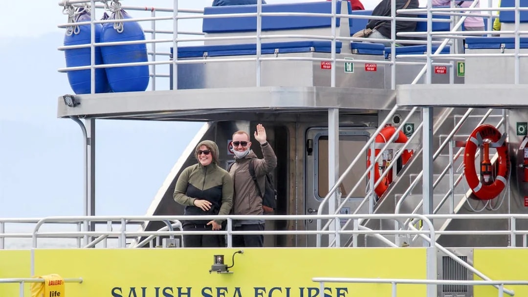 Guests waving on the Salish Sea Eclipse catamaran deck.