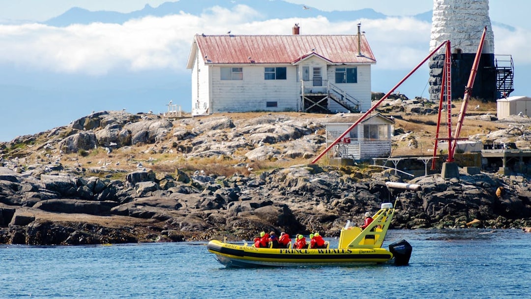 Prince of Whales boat with passengers in red life jackets near a rocky island with a lighthouse.