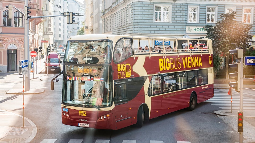 Vienna HopOn HopOff bus on city street with tourists on upper deck.