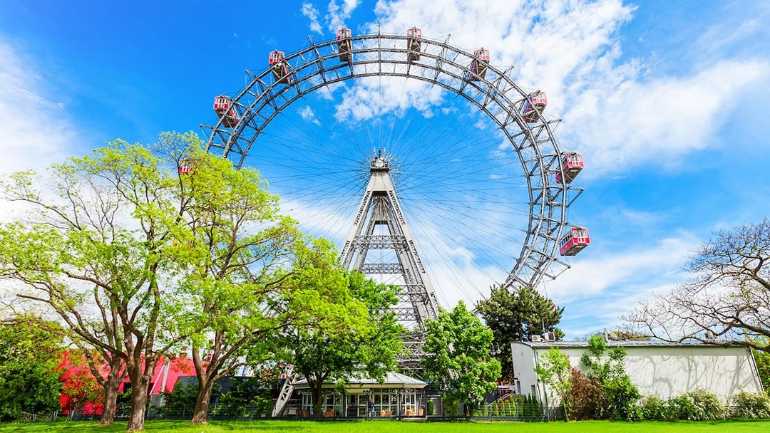 Blumenrad Ferris Wheel in Vienna with lush green trees and blue sky.