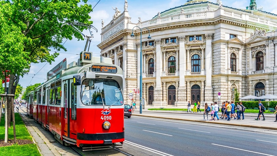 Red tram in front of Vienna's Burgtheater, Austria, with people walking nearby.