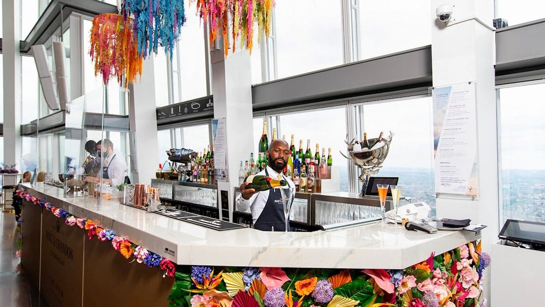Bartender serving champagne at The Shard's bar with city view in London.