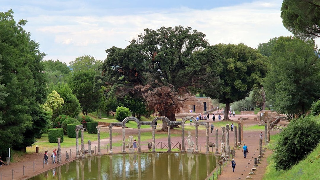Reflecting pool and ancient ruins at Tivoli Villae, Italy, with visitors walking nearby.