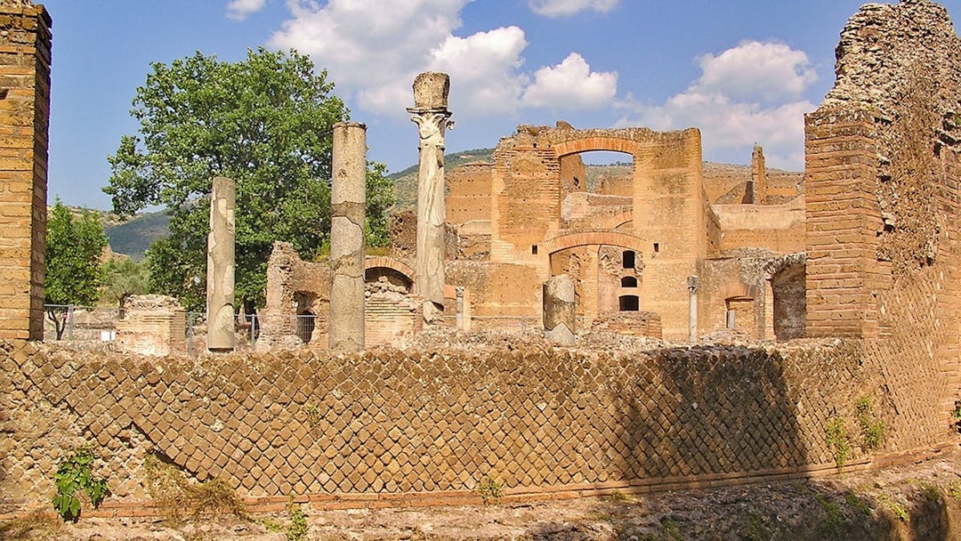 Ancient ruins and columns at Tivoli Villae, Italy, with a backdrop of trees and hills.