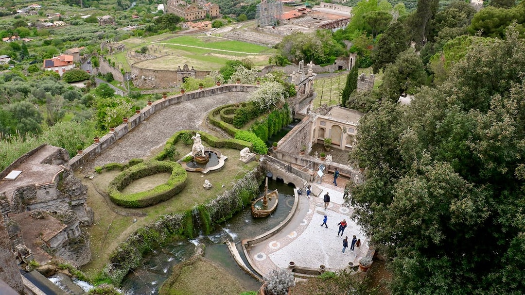 Tourists walking through the gardens of Villa d'Este in Tivoli, Italy, with fountains and sculptures.