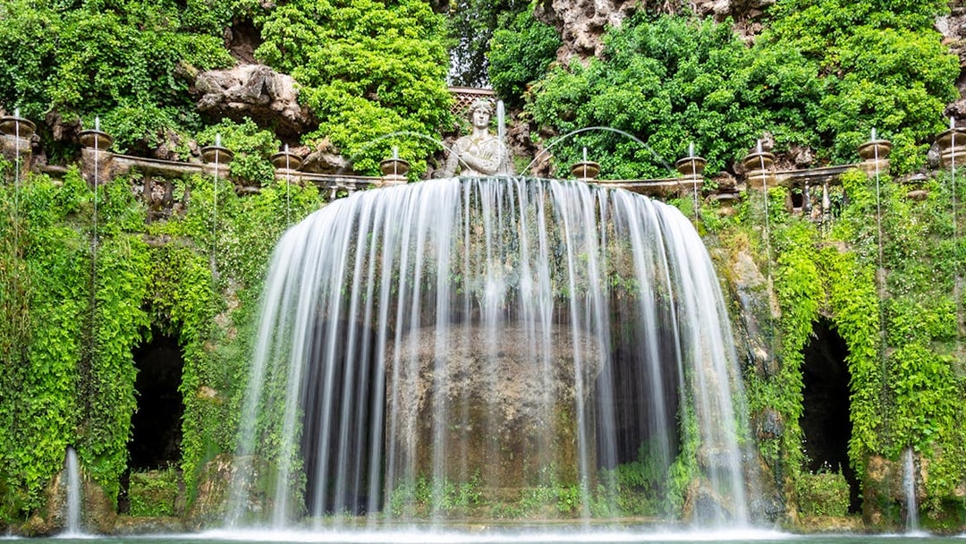 Villa d’Este waterfall with lush greenery and classical statue in Tivoli, Italy.