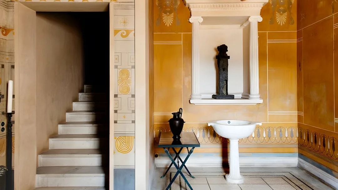 Interior of Villa Kerylos with ornate wall designs, a staircase, and classical decor.
