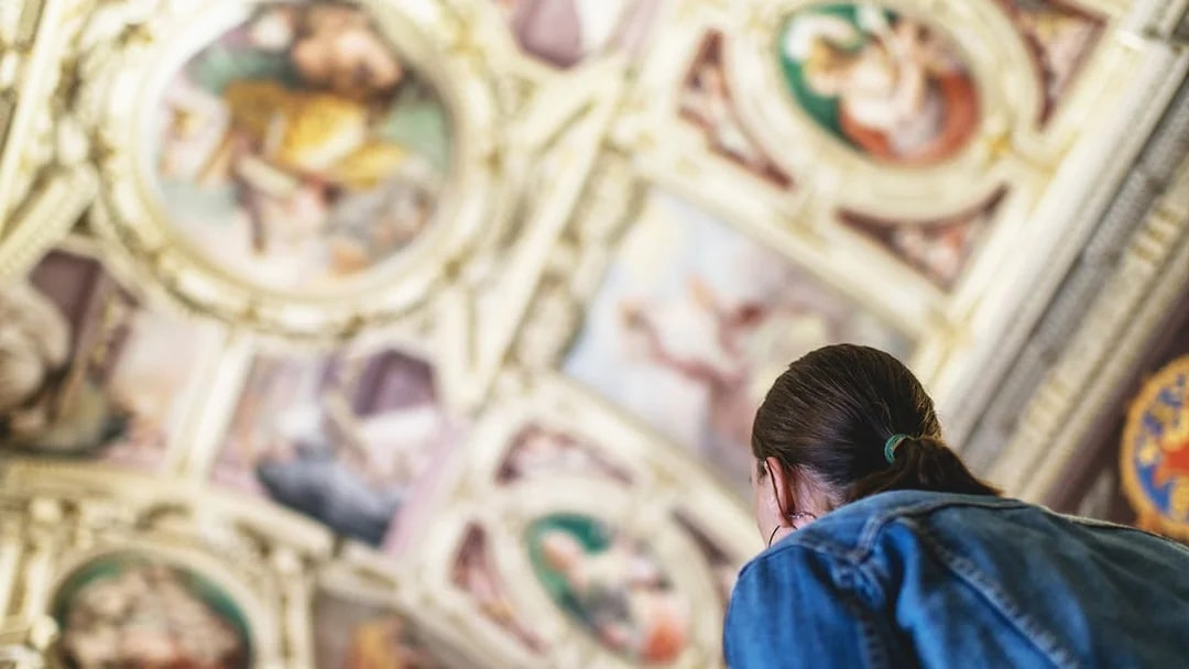 Visitor admiring ceiling artwork in the Vatican Museums.