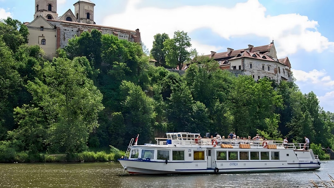Sightseeing boat on Vistula River near historic monastery in Krakow, Poland.
