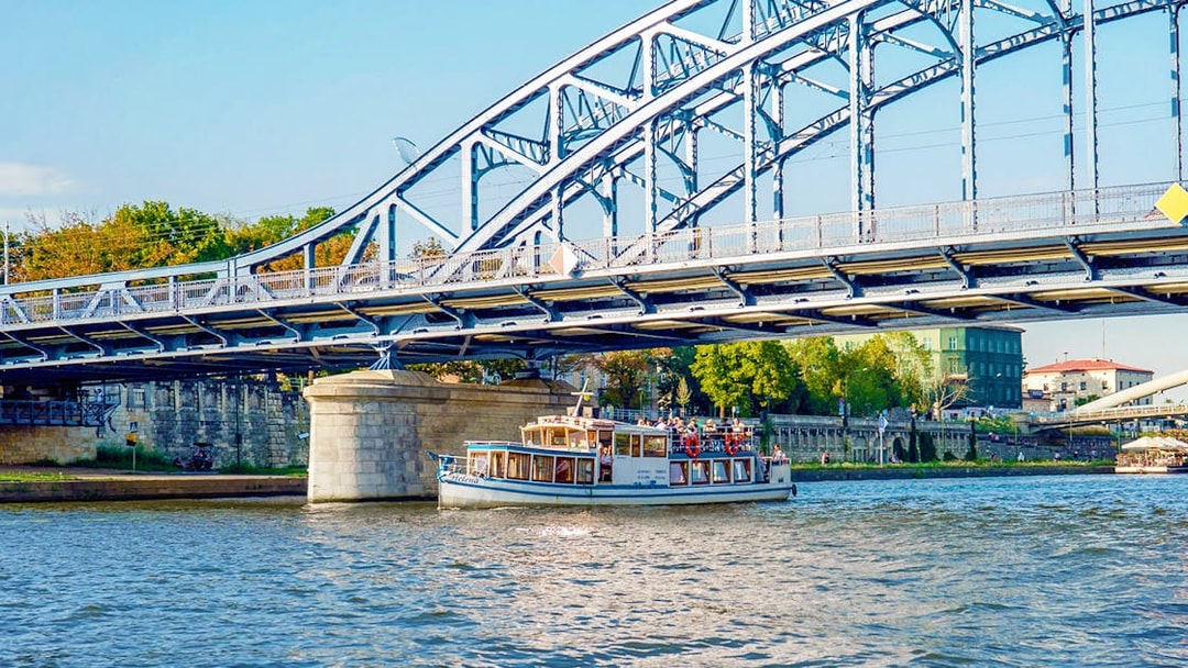 Boat cruising under a steel bridge on the Vistula River during a Cracow city tour.