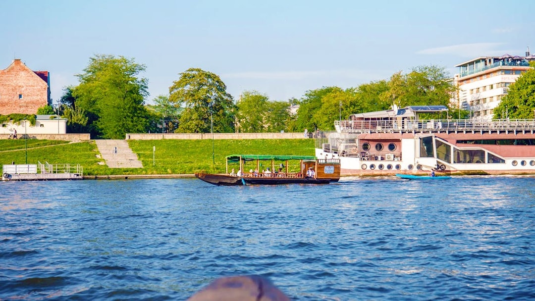 Boat on Vistula River during Cracow city tour, with riverside view and greenery.