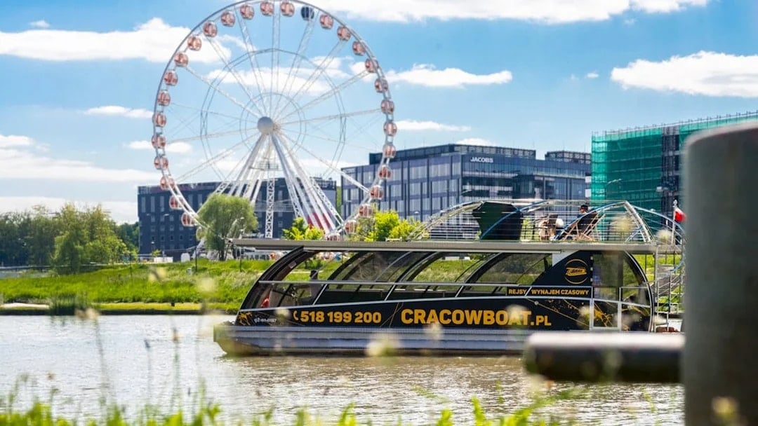 Catamaran on Vistula River with ferris wheel in Krakow background.