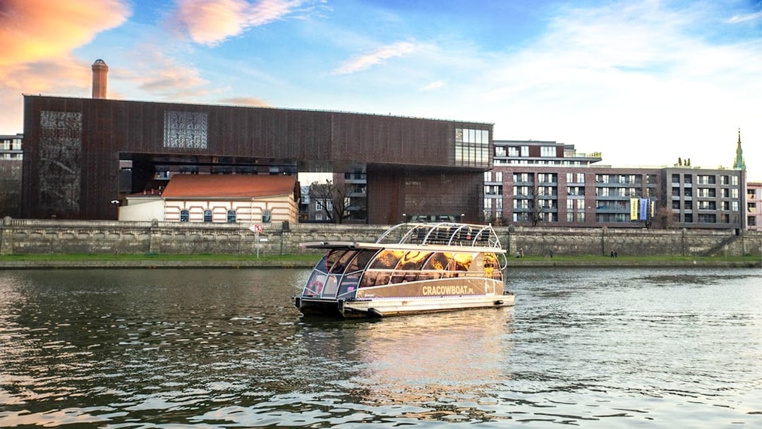 Catamaran cruising on the Vistula River in Krakow with modern buildings in the background.