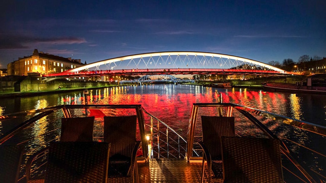 Catamaran view of illuminated bridge over Vistula River at night in Krakow.