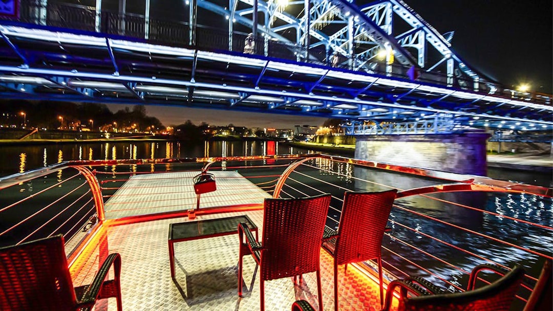 Cruise deck view under illuminated bridge on Vistula River at night in Krakow.