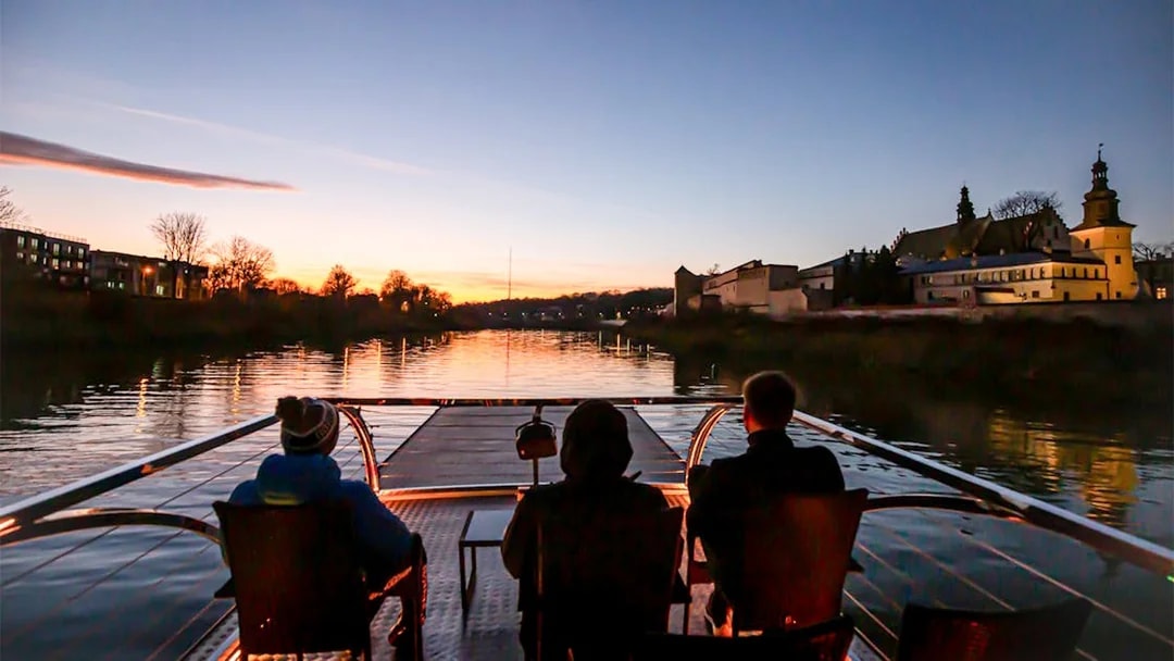 Guests enjoying a night cruise on the Vistula River in Krakow, viewing city lights and landmarks.