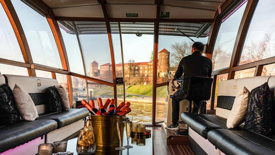 Interior view of a catamaran on the Vistula River Cruise in Krakow, with Wawel Castle visible through the windows.