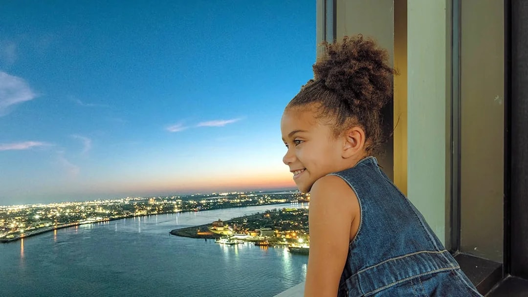 Child enjoying sunset view from Vue Orleans Observation Deck over Mississippi River.