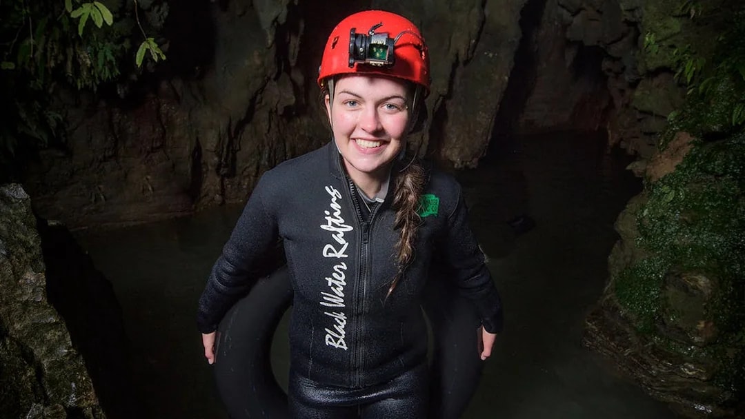 Person in wetsuit and helmet holding an inner tube in Waitomo cave for black water rafting experience.