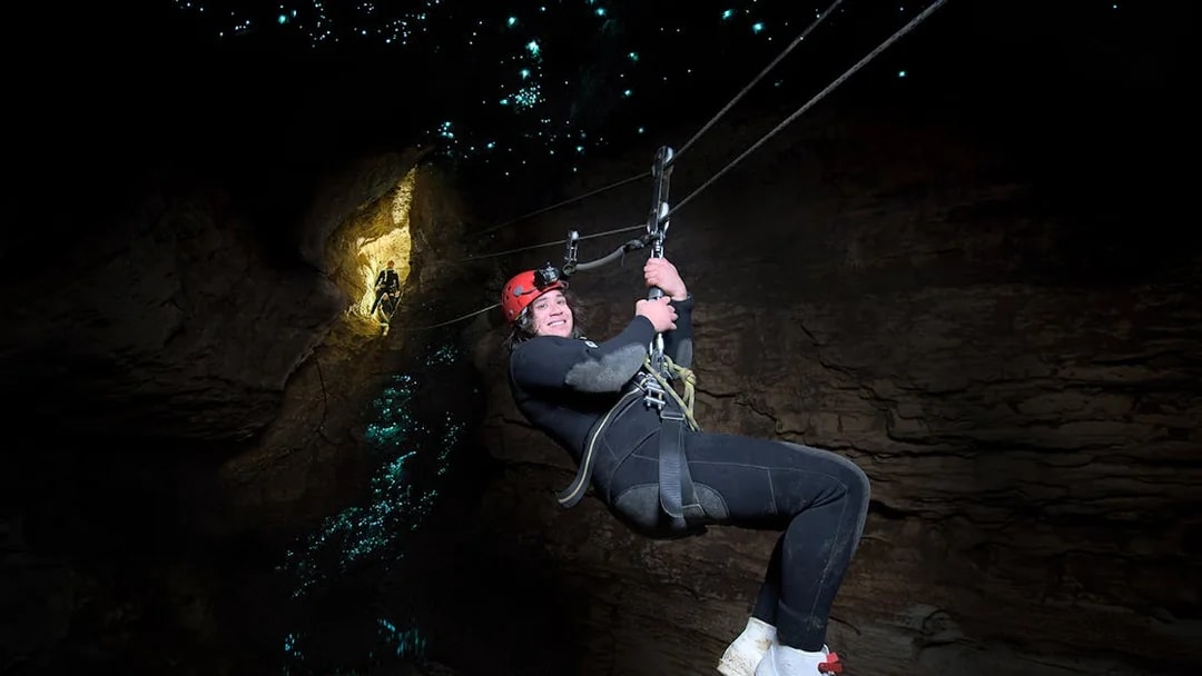 Person ziplining in Waitomo Cave with glowworms illuminating the cave walls.