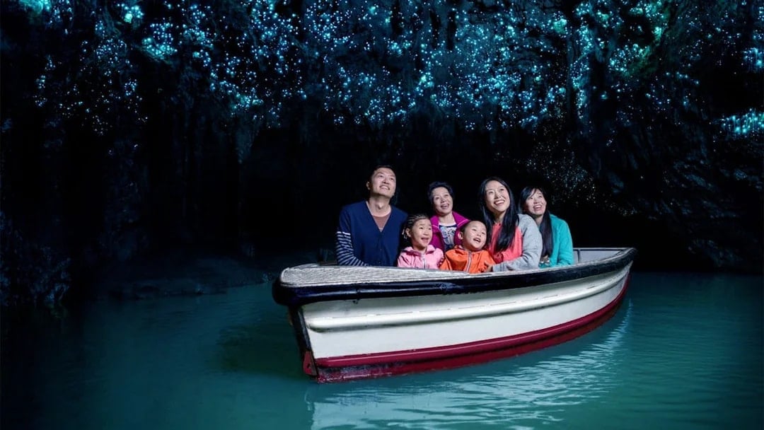 Group enjoying boat tour in Waitomo Glowworm Caves, New Zealand, with glowing ceiling.