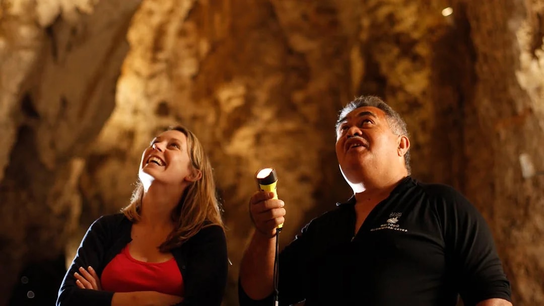 Visitors exploring Waitomo Glowworm Caves with a guide holding a flashlight.