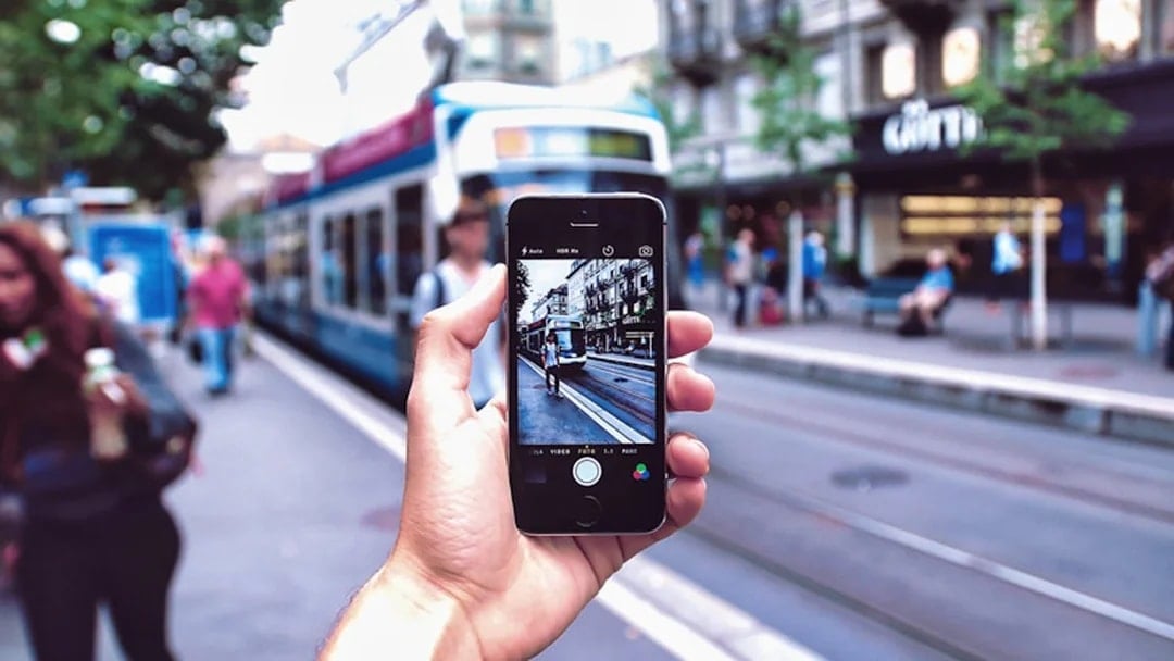 Person holding a smartphone capturing a tram on a street in Amsterdam.