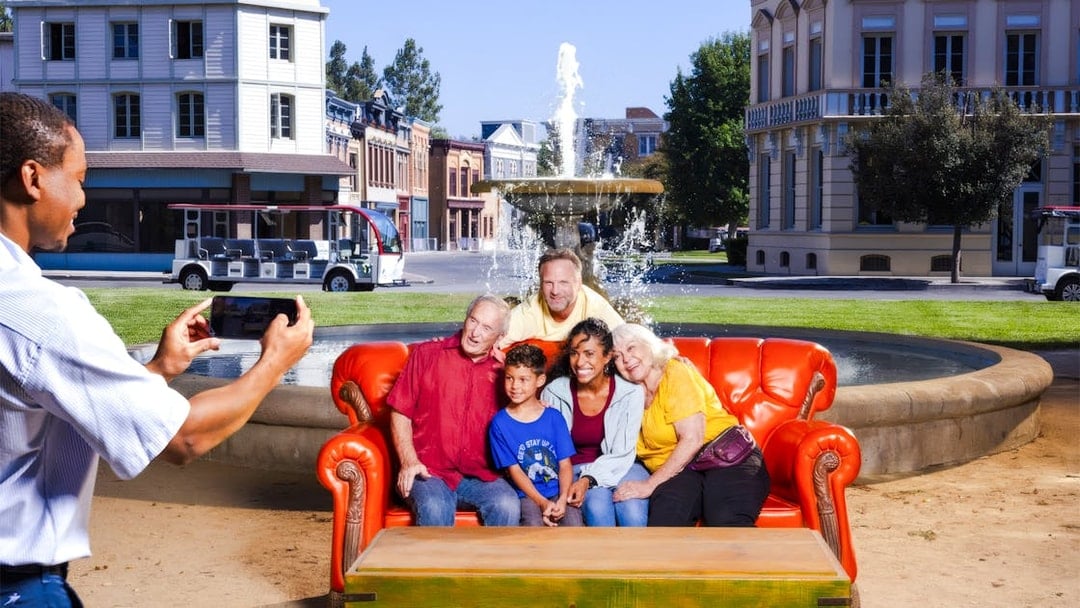 Six people on the iconic orange couch from Friends, posing for a photo in front of a fountain.