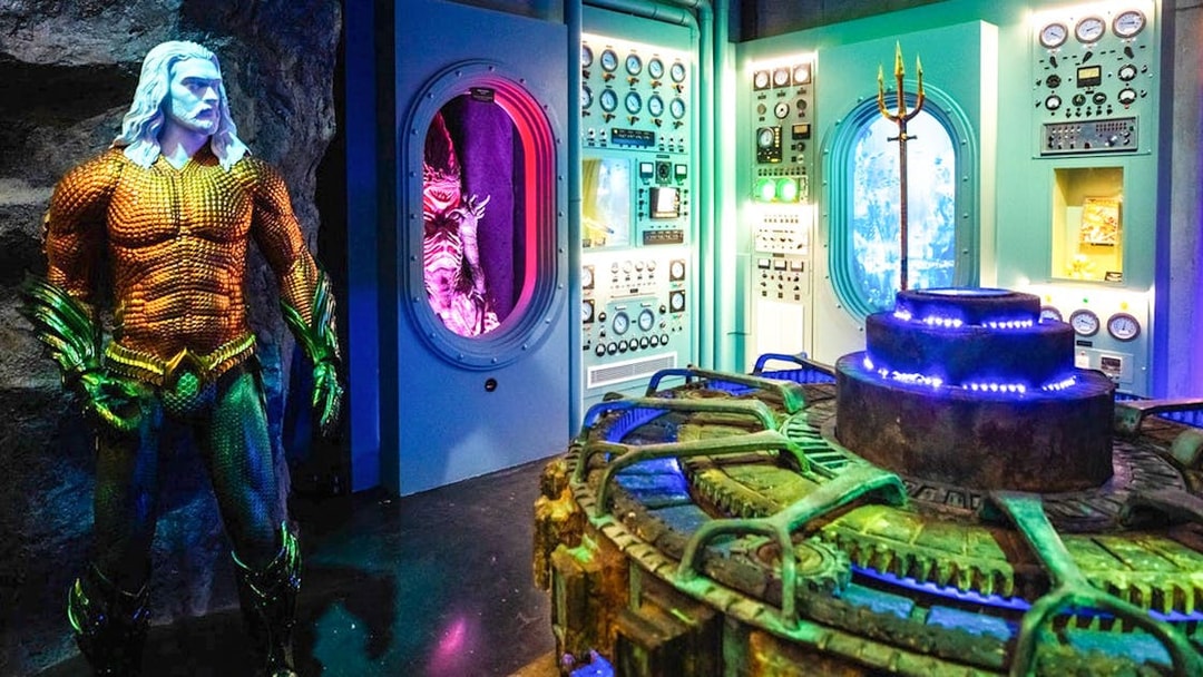 Statue of Aquaman in front of a control room with colorful lights and machinery.