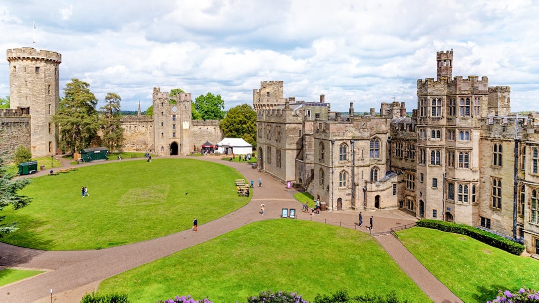 Warwick Castle courtyard with historic stone buildings and lush green lawn.