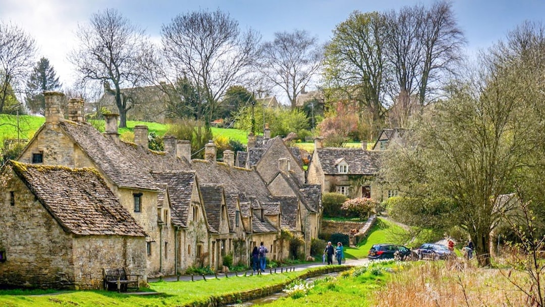 Arlington Row cottages in Bibury Village, Cotswolds, with visitors walking nearby.