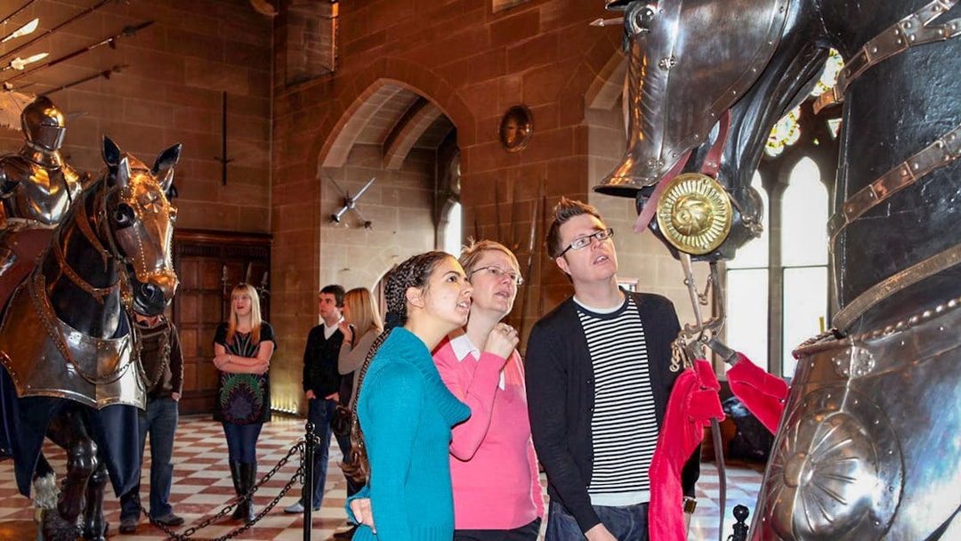 Visitors observing knight armor display at Warwick Castle.