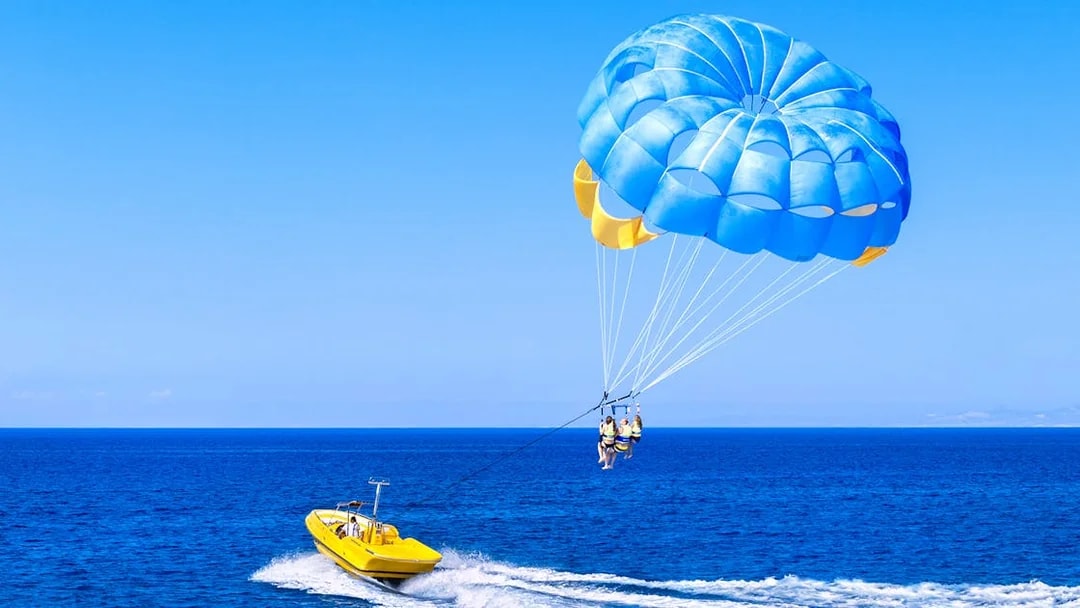 Parasailing over the ocean in Pantai Cenang with a yellow boat.