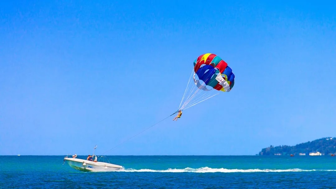 Parasailing over the ocean in Pantai Cenang with a colorful parachute.