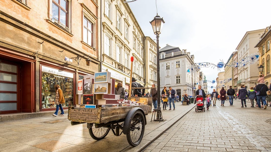 Street scene in Kraków's Old Town with market cart and pedestrians.