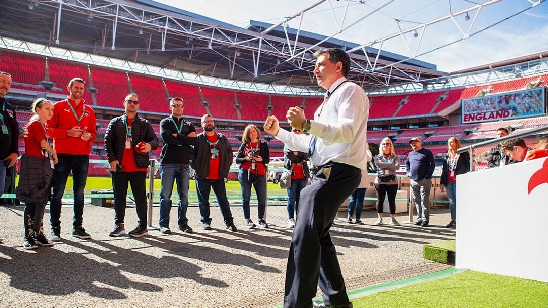 Tour group at Wembley Stadium, London, with guide explaining features.
