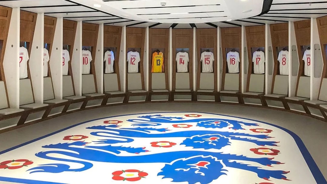 Wembley Stadium dressing room with England football jerseys displayed.