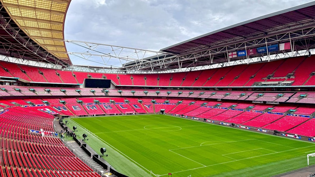 Wembley Stadium interior with empty red seats and green pitch, London.