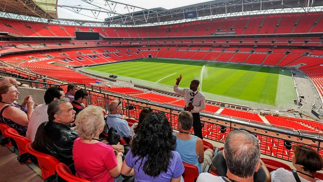 Guide speaking to visitors at Wembley Stadium with view of the field.