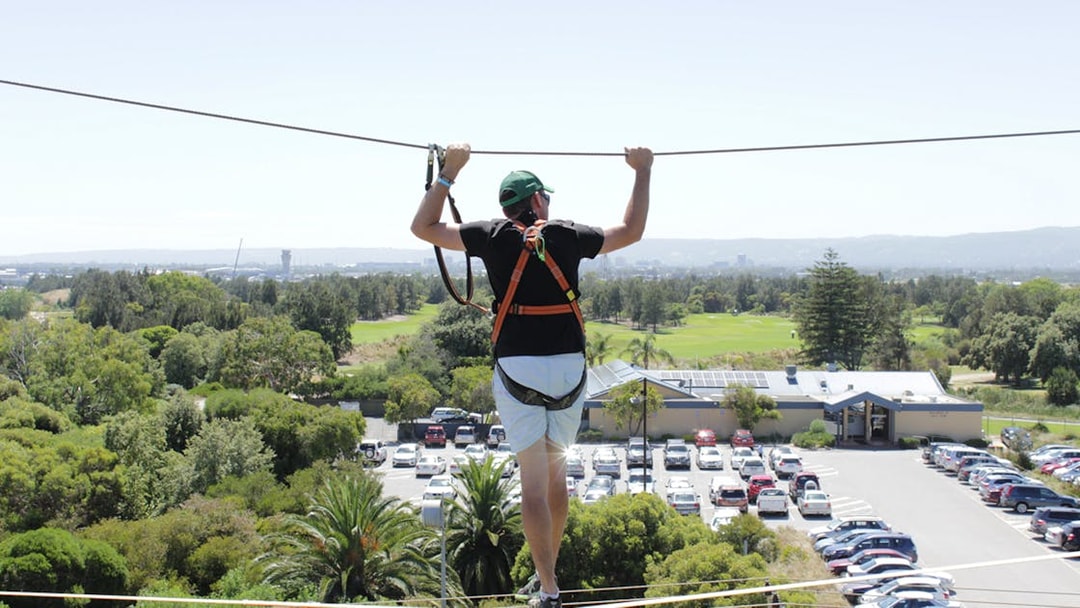 Person on high ropes course at West Beach Adventure, overlooking greenery and parking area.