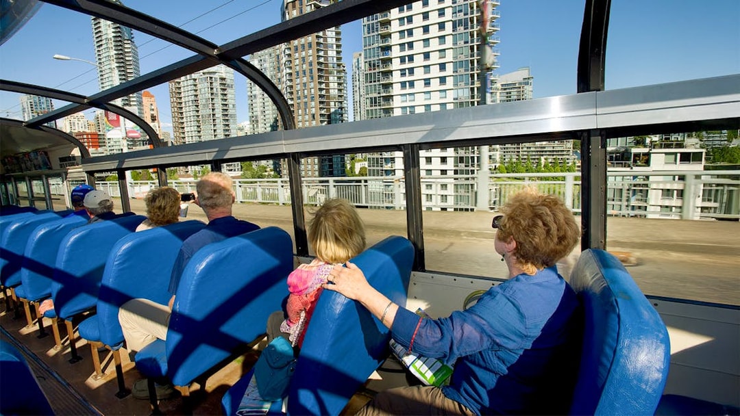 Tourists on Vancouver hop-on hop-off bus viewing city skyscrapers.