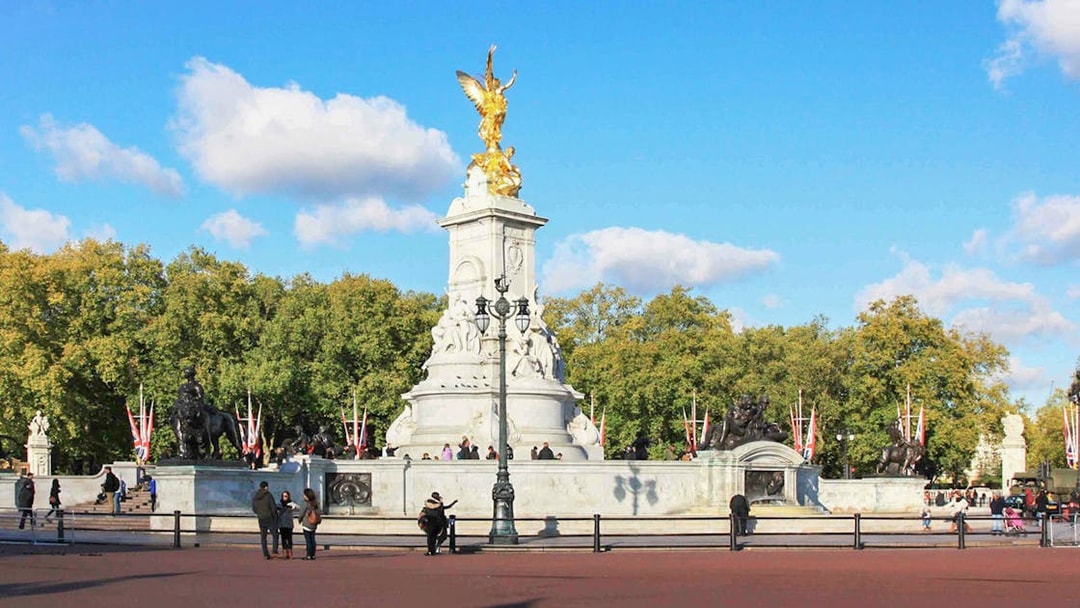 Victoria Memorial near Buckingham Palace, London, with tourists and trees in the background.