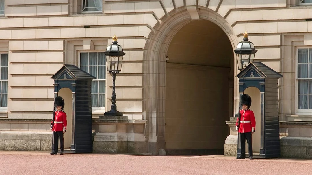 Guards in red uniforms at Buckingham Palace entrance, London.