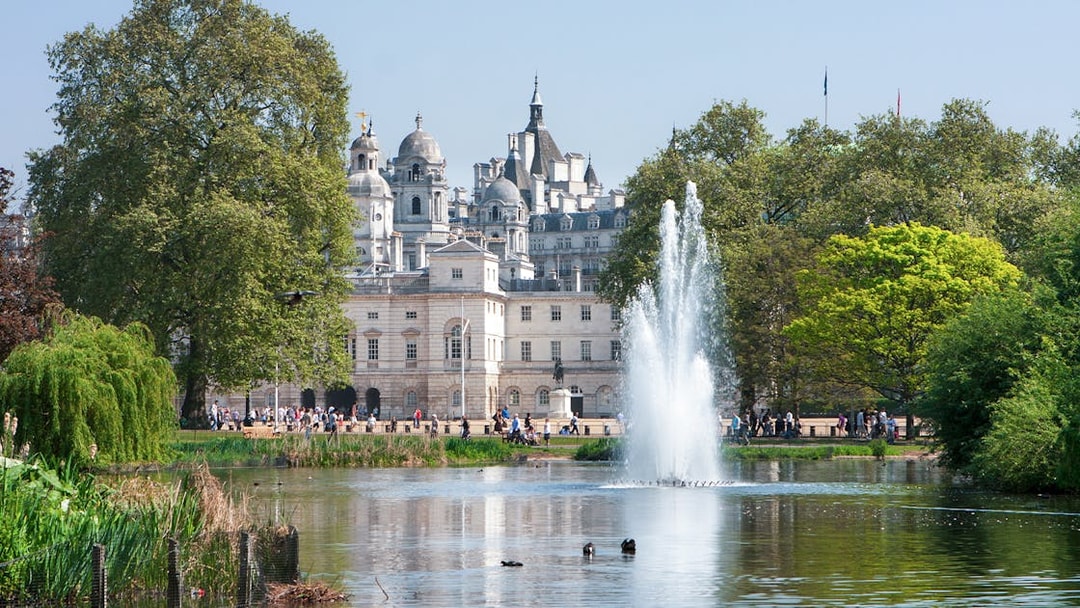 Fountain and trees in St James's Park with historic buildings in London.