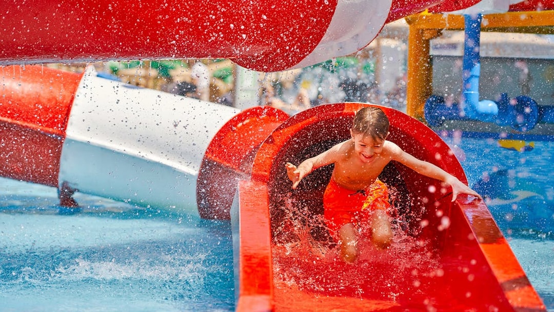 Boy sliding down a red water tube at Wet World Water Park.
