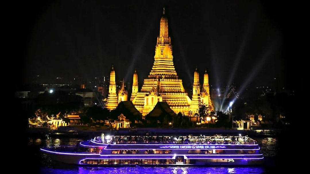 River cruise boat passing Wat Arun temple in Bangkok at night.